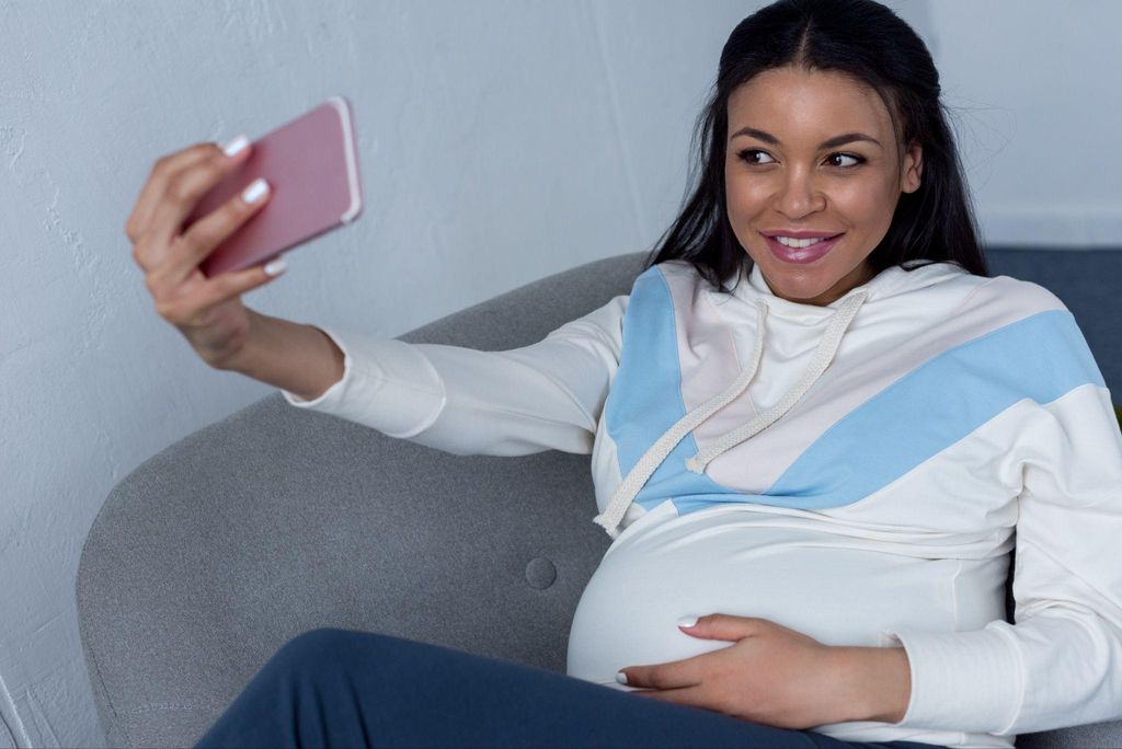 Pregnant woman takes selfie at home.