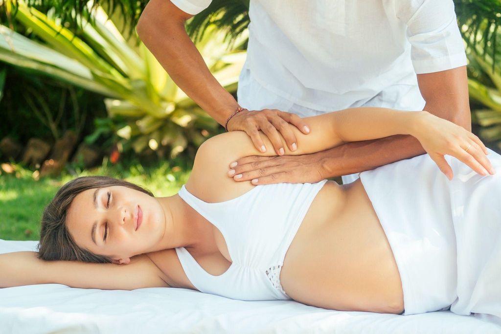 A pregnant woman enjoys an antenatal massage while lying on a massage table in a garden.