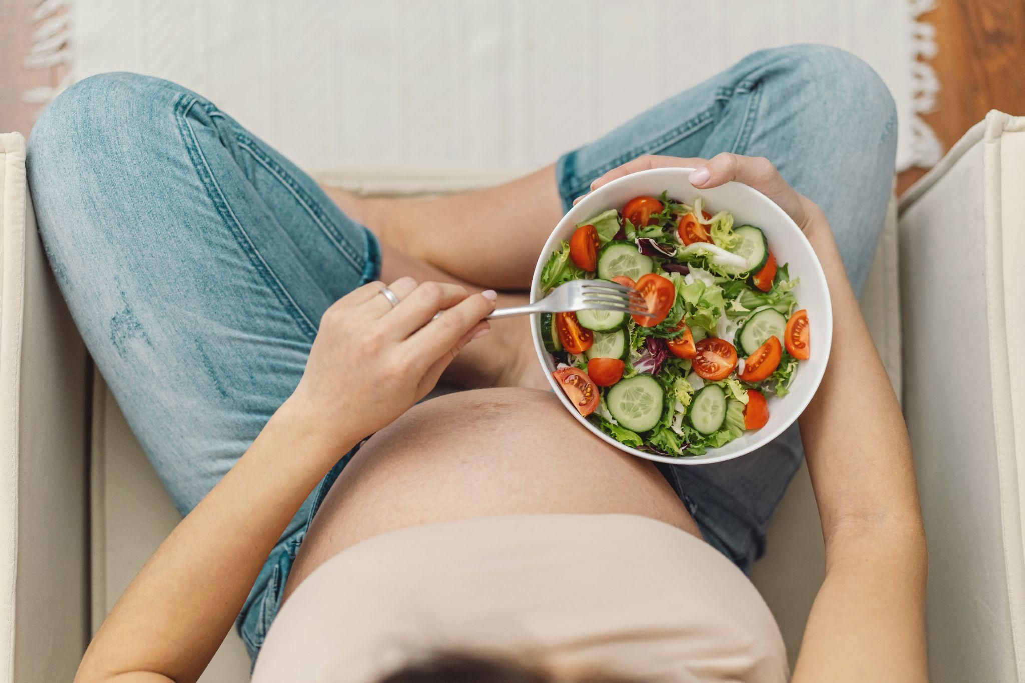 Smiling pregnant woman eating a healthy salad at home.