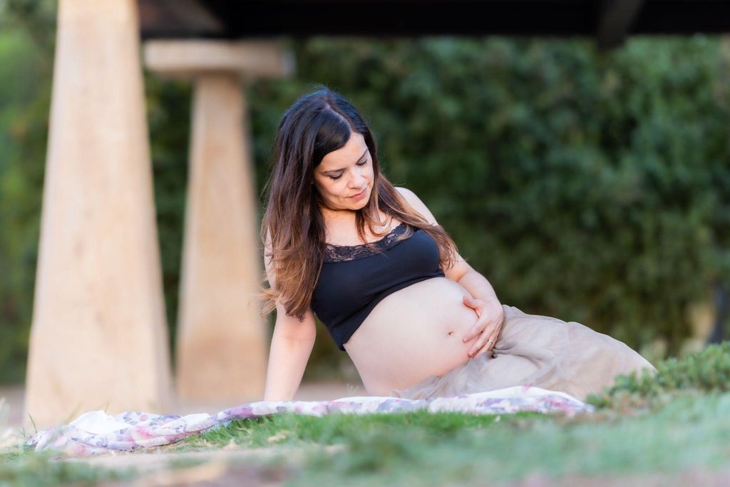 A mum-to-be relaxing on a blanket in the park, focusing on her baby’s antenatal movements.