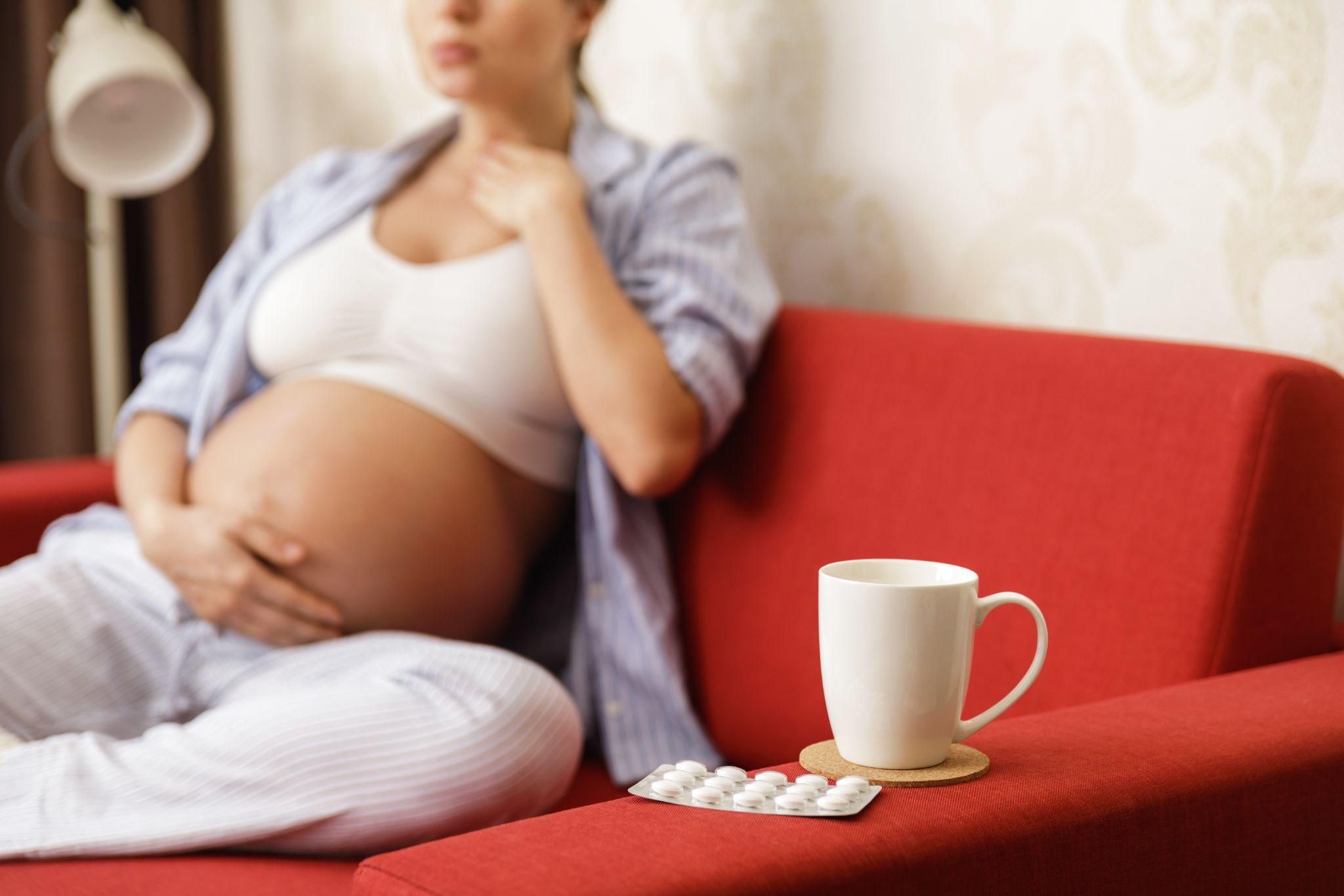 Pregnant woman takes medication for sore throat on couch.