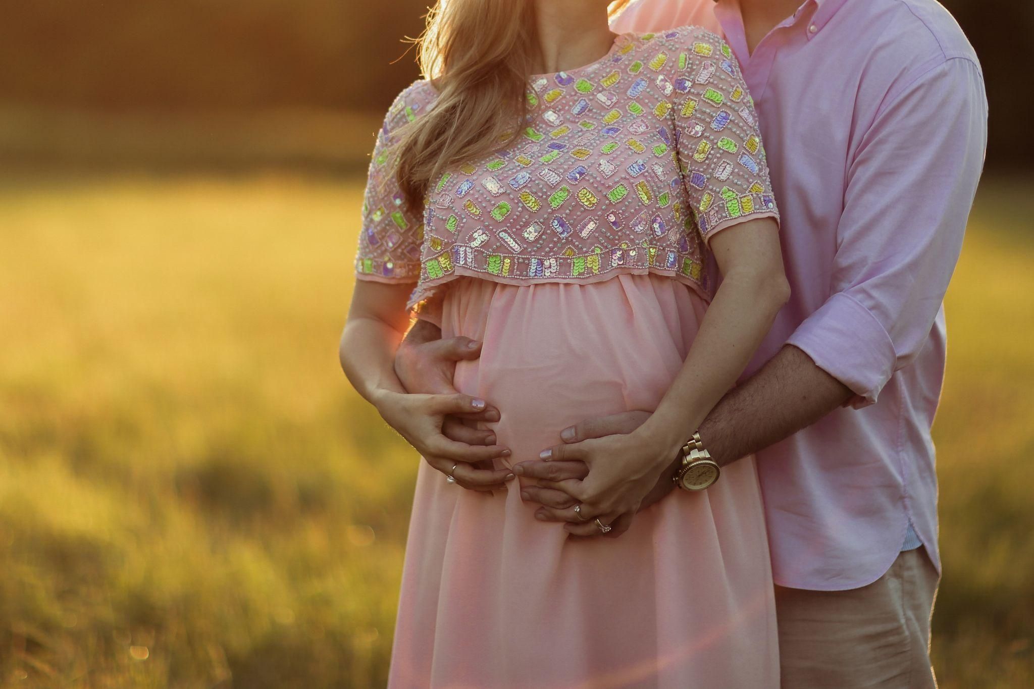 Pregnant woman smiling in a garden during a maternity photoshoot.