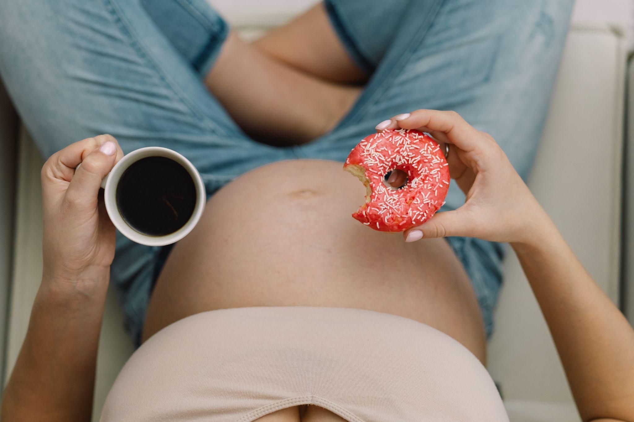 Pregnant woman eating doughnut and drinking coffee.