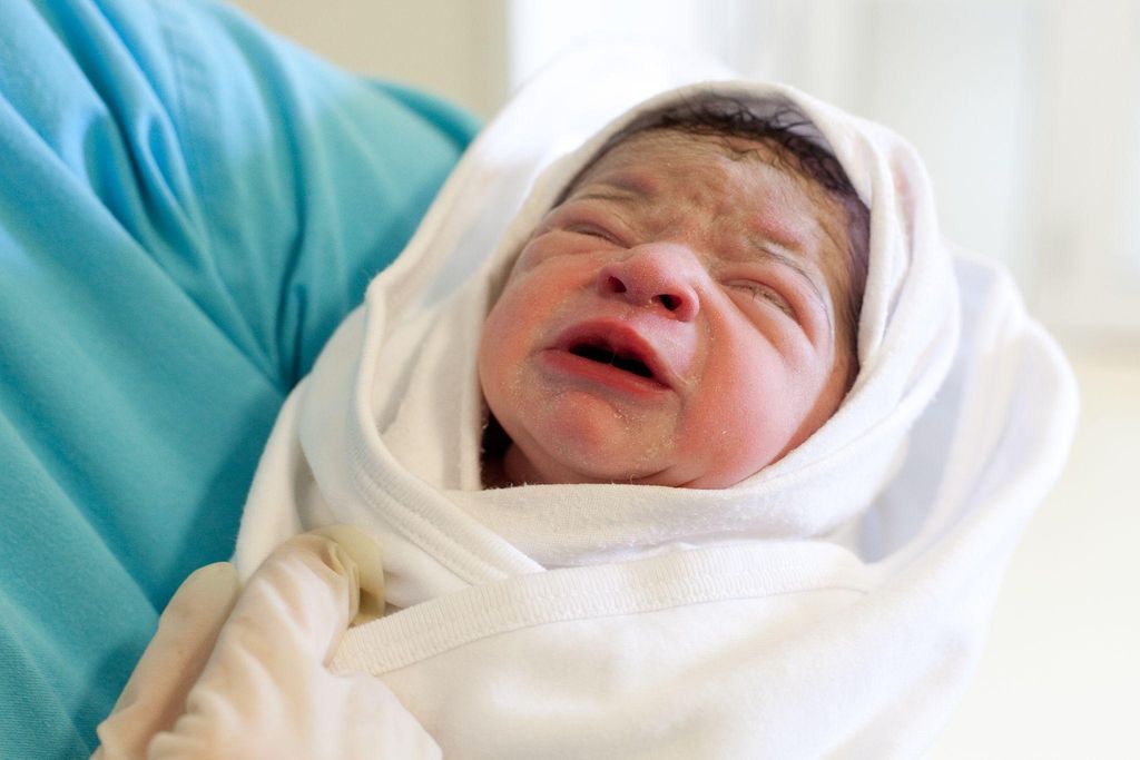 Crying newborn is swaddled and held by midwife in hospital.