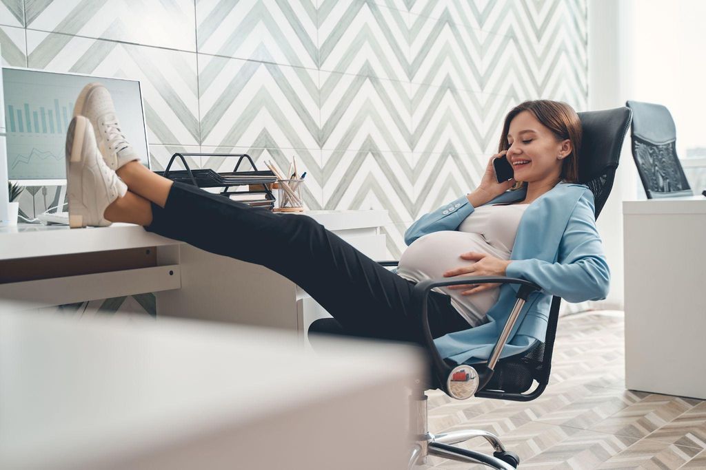 A pregnant woman sitting and resting during work hours, focusing on good posture and wearing comfortable shoes.