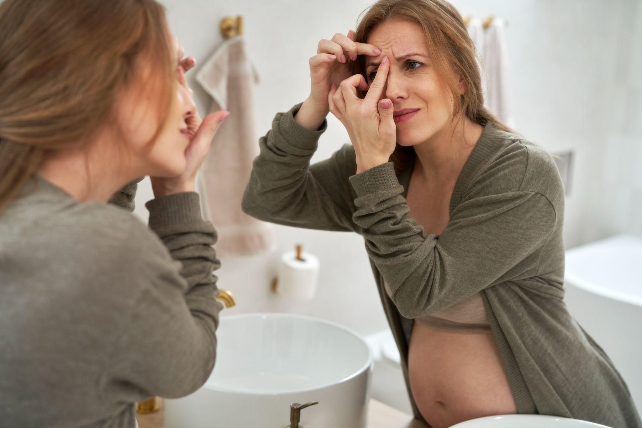 A pregnant woman applying skincare serum to her face to address pigmentation issues during pregnancy.