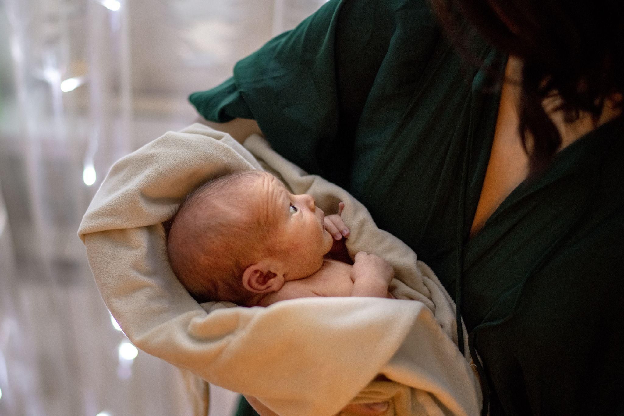 A smiling mother holding her newborn in a hospital bed after a Caesarean section.