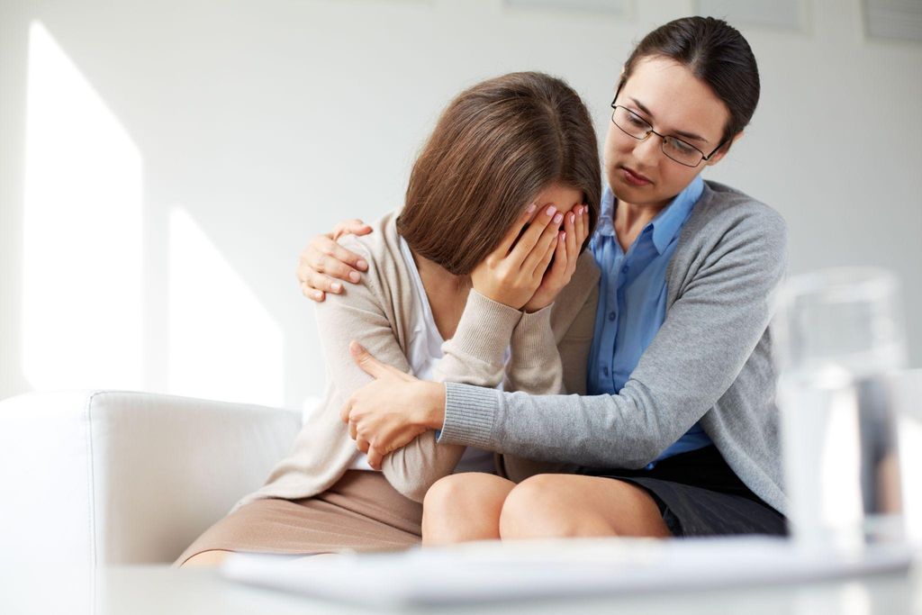 A healthcare professional gently holding a patient's hand during a sensitive conversation about pregnancy loss.