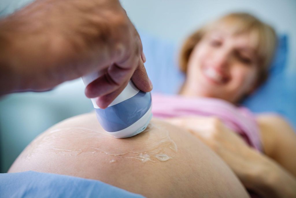 Expectant mother looking at her doctor’s ultrasound wand during an antenatal appointment.