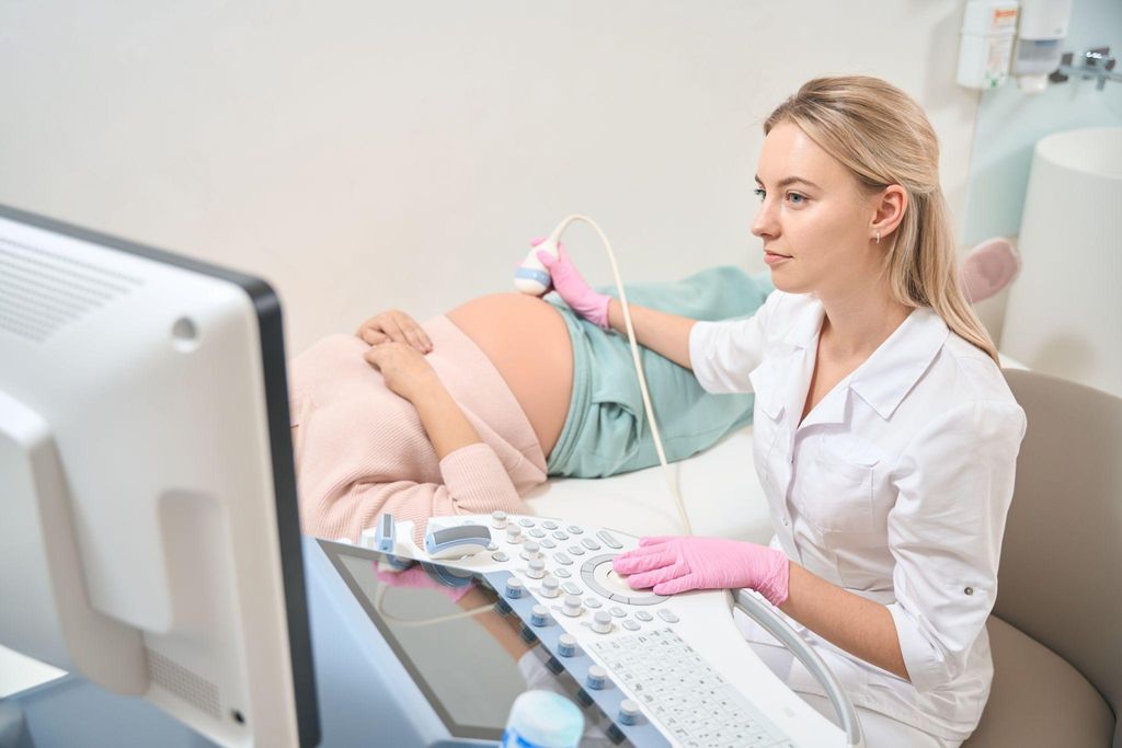 Pregnant woman has ultrasound scan with sonographer during antenatal appointment.