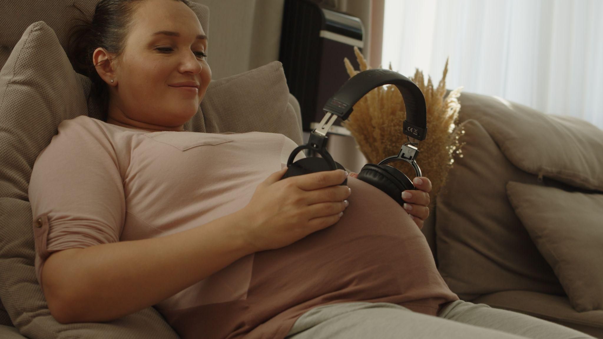 A calm pregnant woman bonding with her baby by playing classical music.