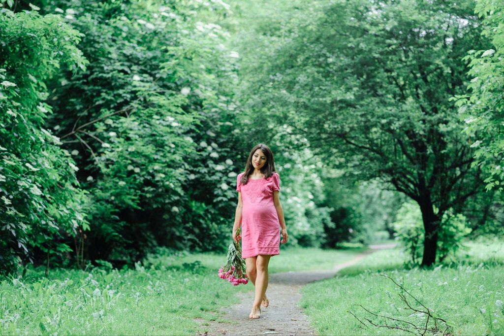 A pregnant woman posing for a maternity photoshoot in a park with soft natural light and a glowing background.