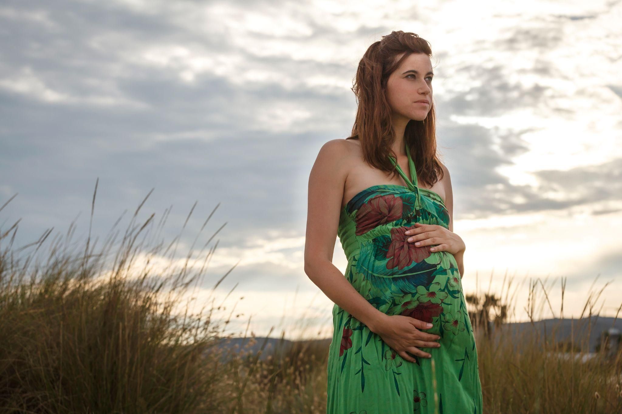 Pregnant woman standing thinking in a field.