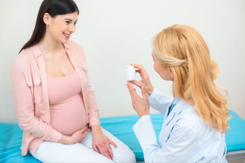 Obstetrician hands pregnant woman a bottle of pills during antenatal appointment.