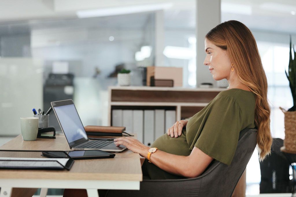 A pregnant woman working on her laptop with a comfortable posture and ergonomic setup to avoid resting the laptop on her bump.