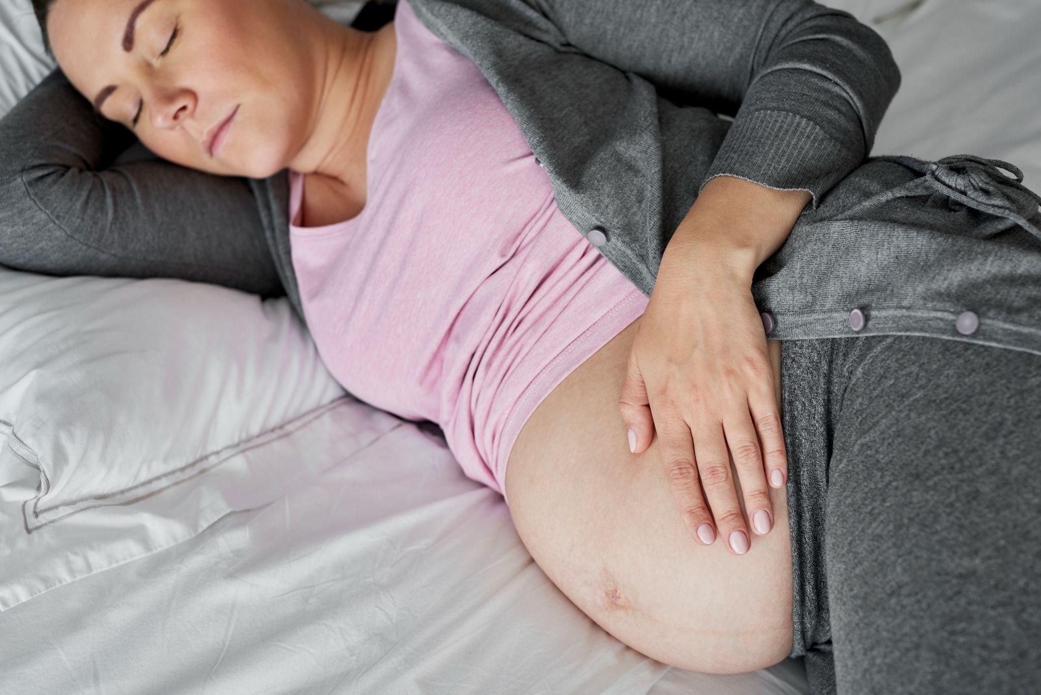 Pregnant woman lying on side in bed, looking tired.