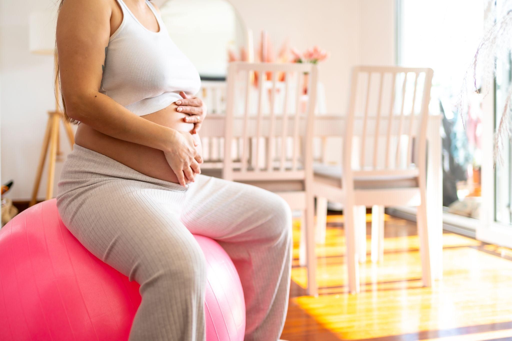 Pregnant woman works out on a birthing ball at home.