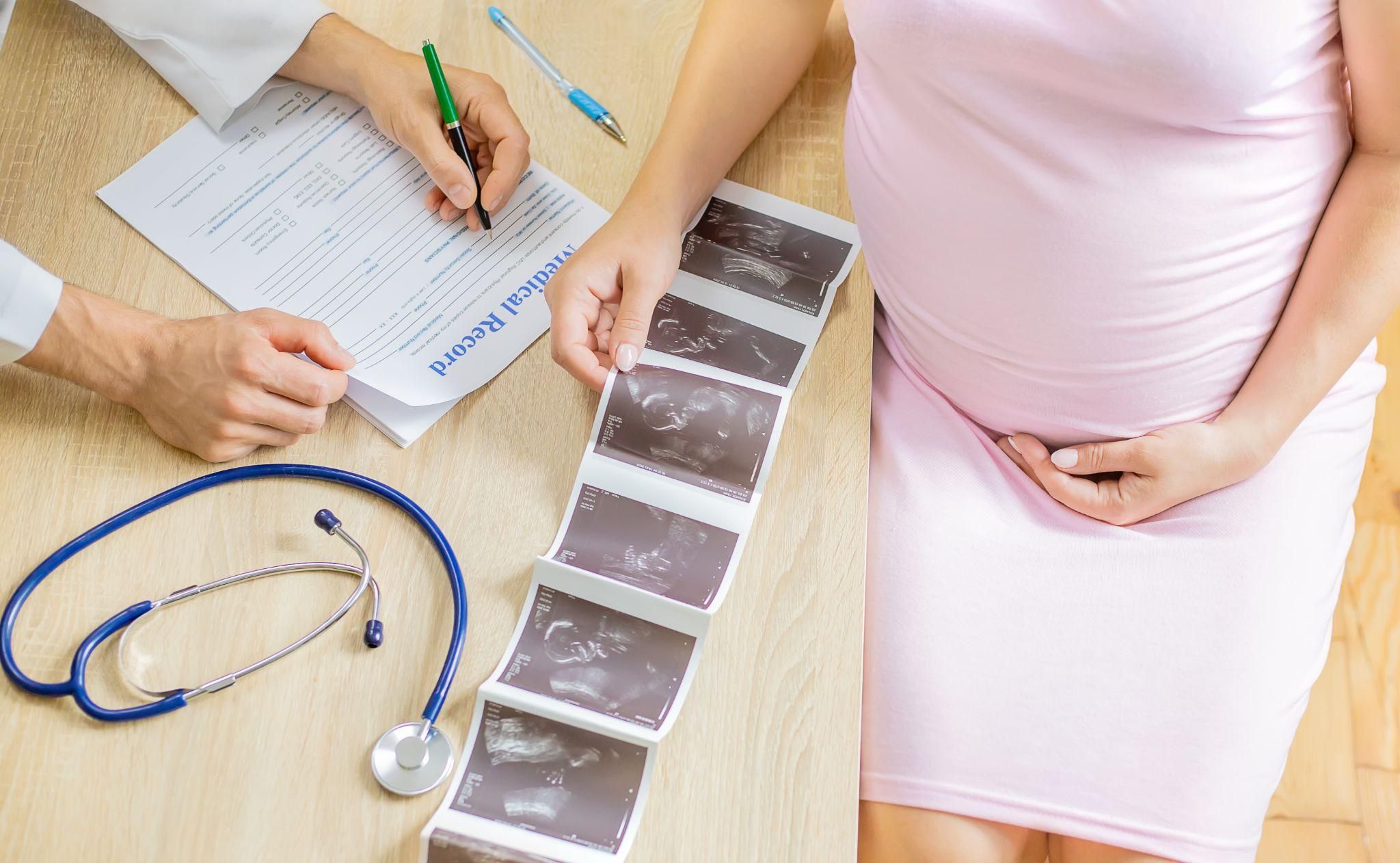 Pregnant woman goes through her medical record and ultrasound photos with a doctor during a second trimester antenatal appointment.