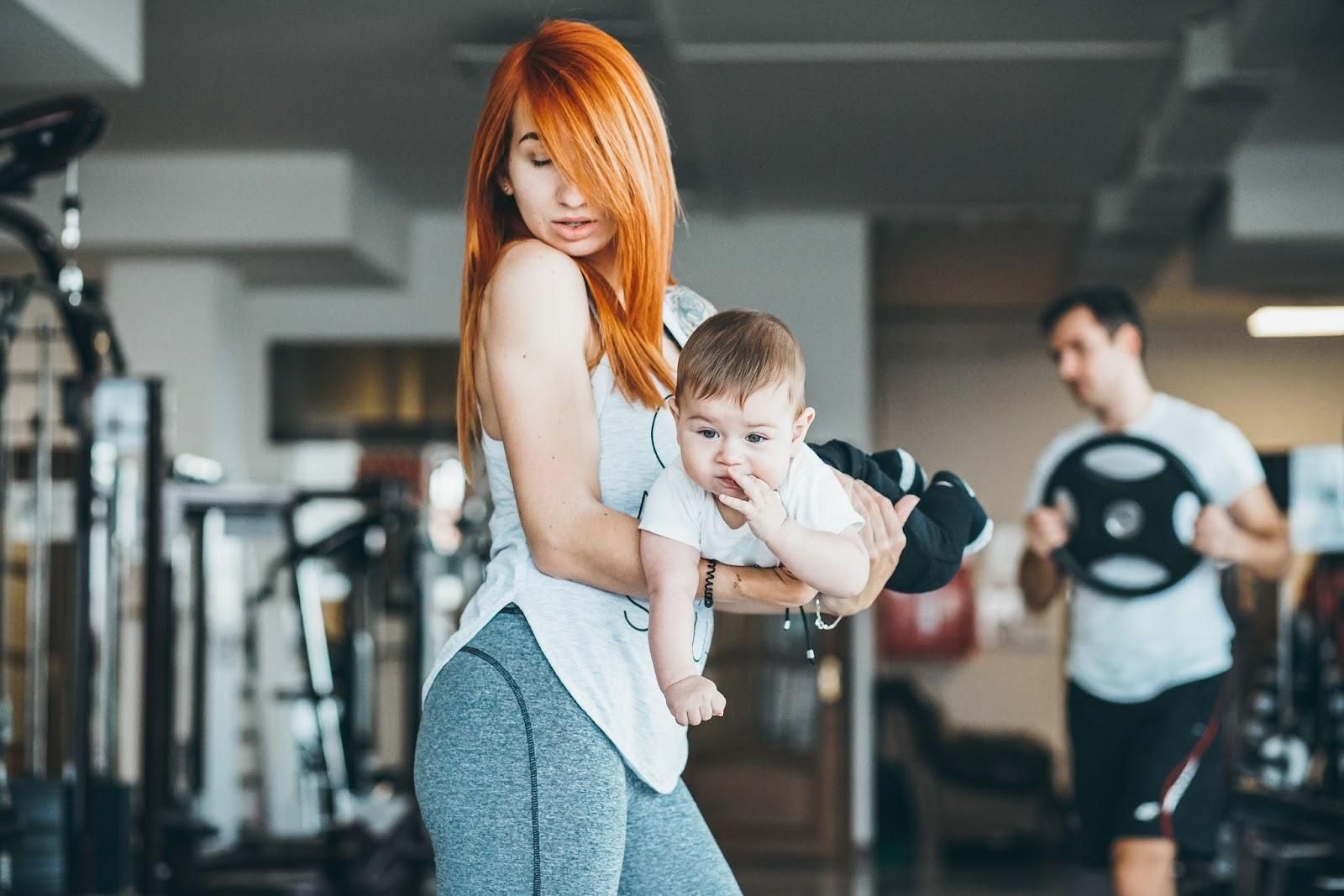 A new mother smiling while holding her baby, reflecting on her postpartum journey and body changes.