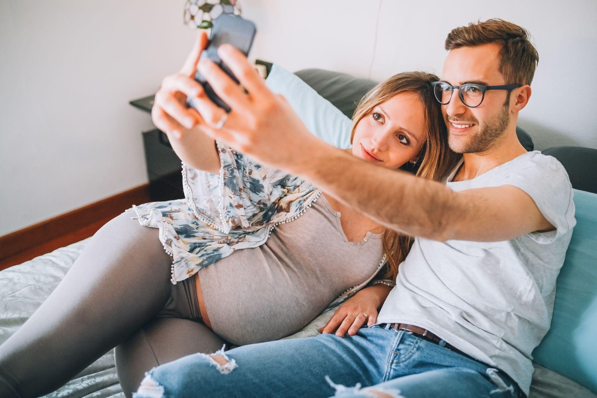 A pregnant couple take a selfie at home.