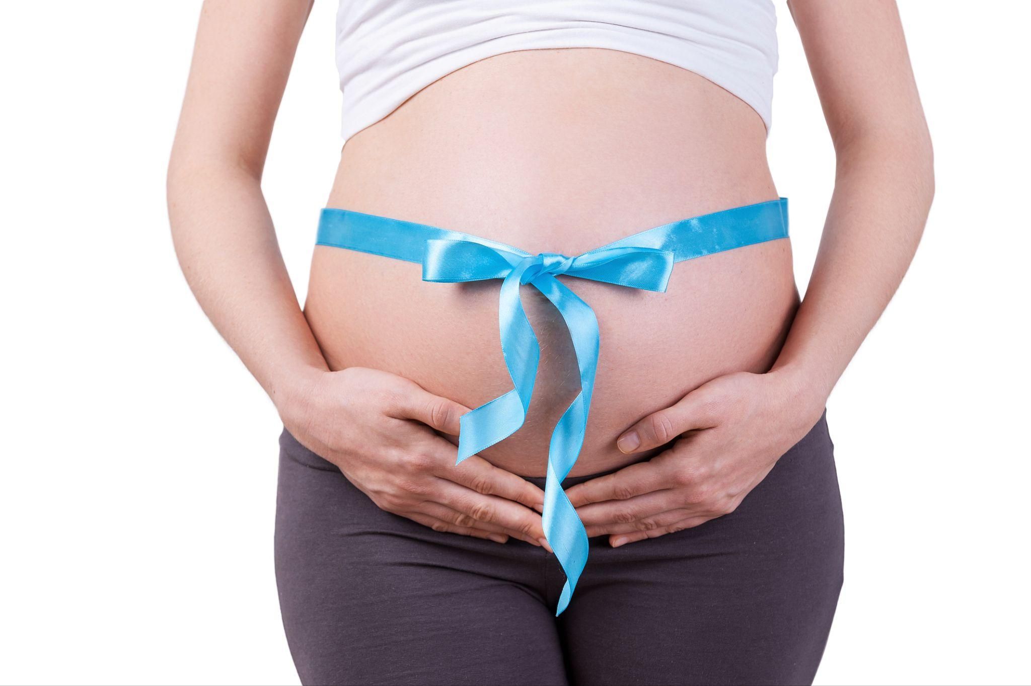 A pregnant woman with a blue ribbon around a heavy, tight bump.