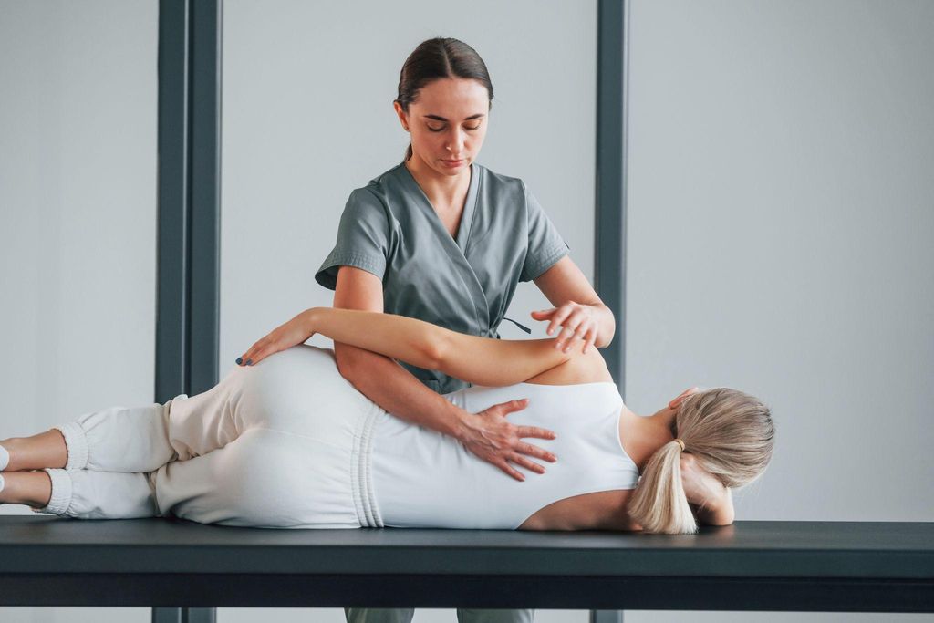 A pregnant woman has her back massaged while lying on her side on a massage table.