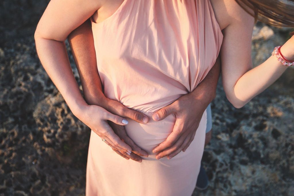 Pregnant woman in a sunlit meadow, embracing her pregnancy with a serene smile.