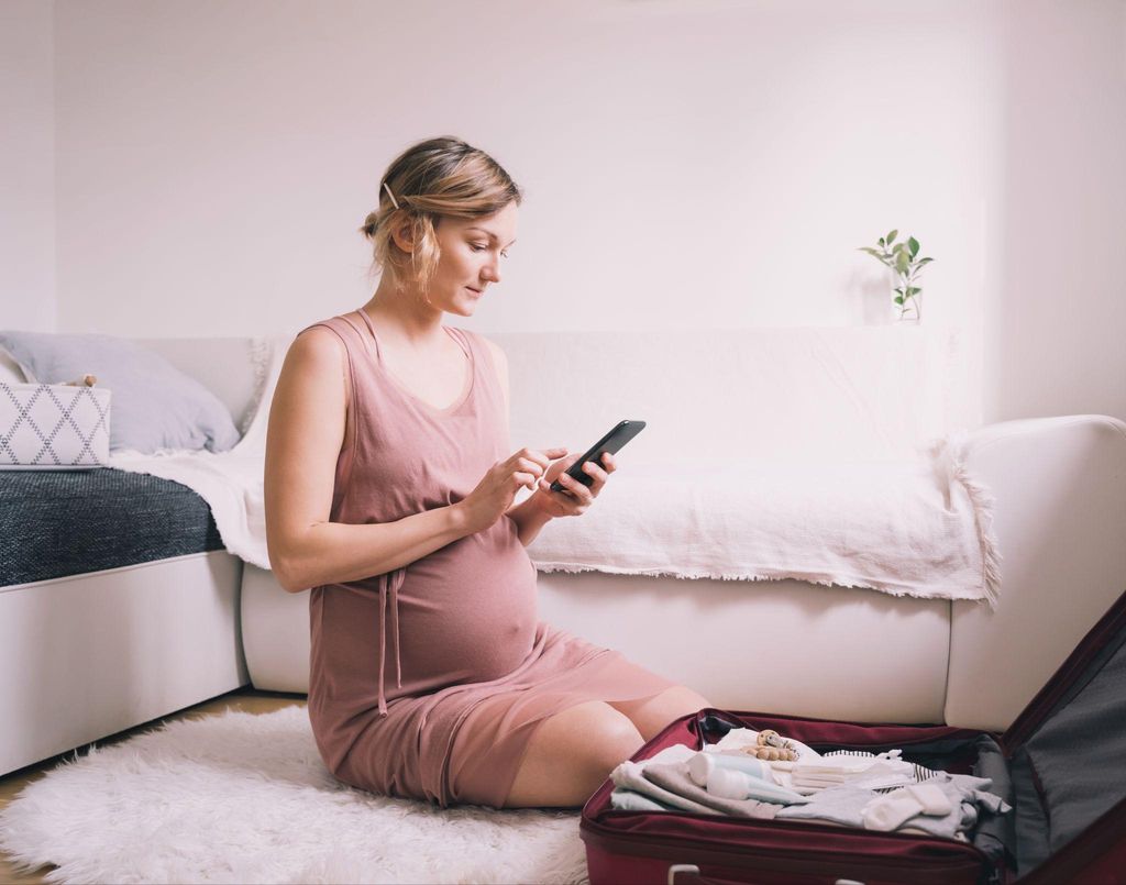 Woman packing bag for hospital bag calls midwife on mobile phone.