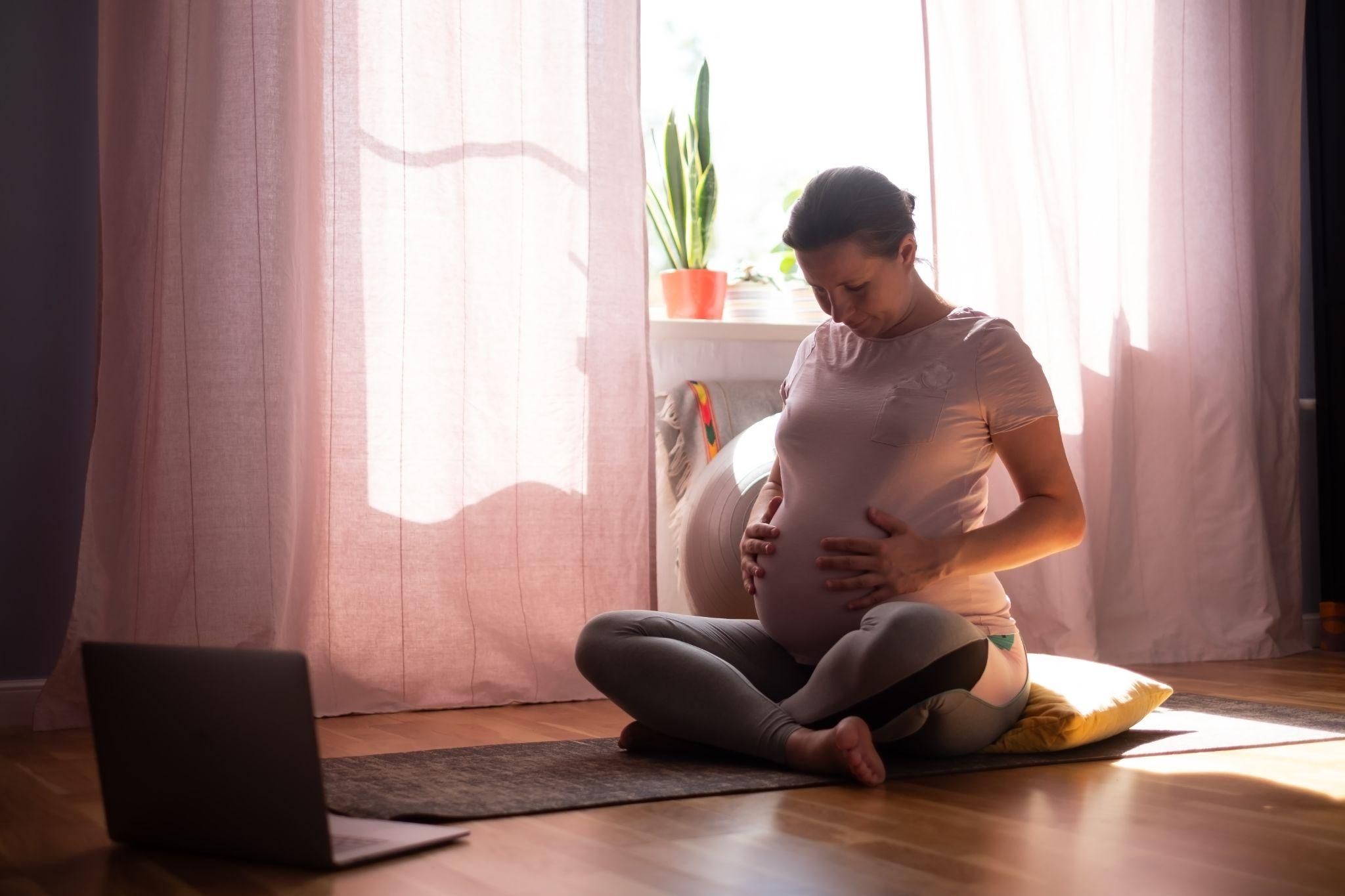 A smiling pregnant woman performing an online antenatal yoga class for better antenatal posture.