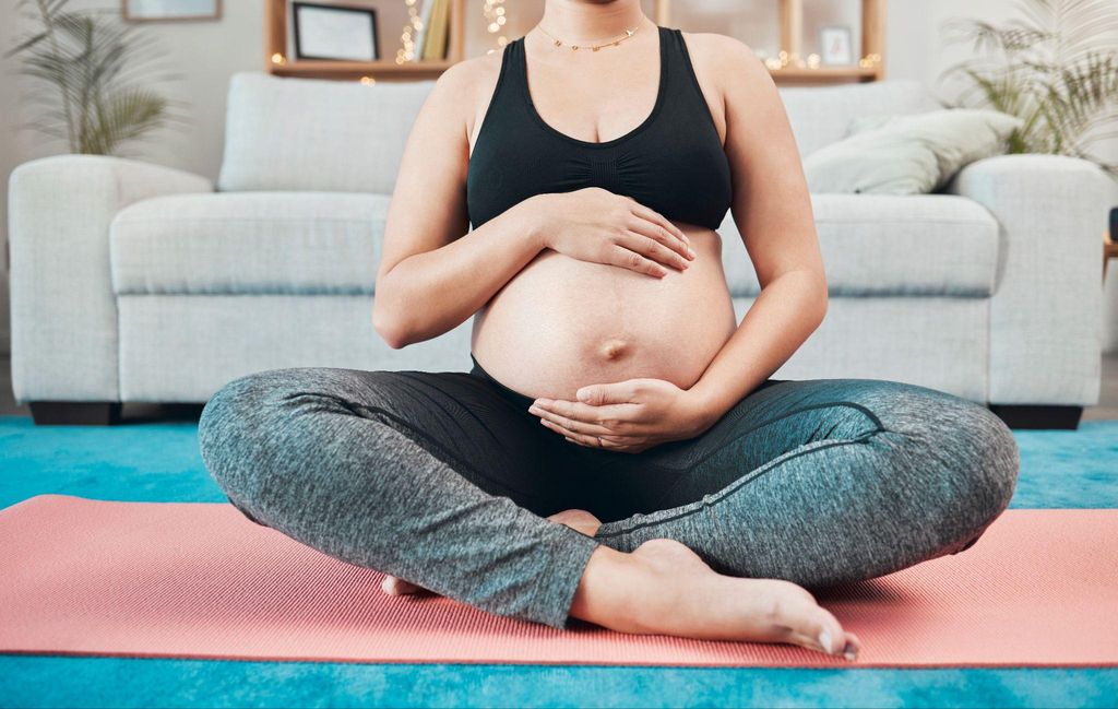 Pregnant woman holds her bump and breathes during yoga practice at home.