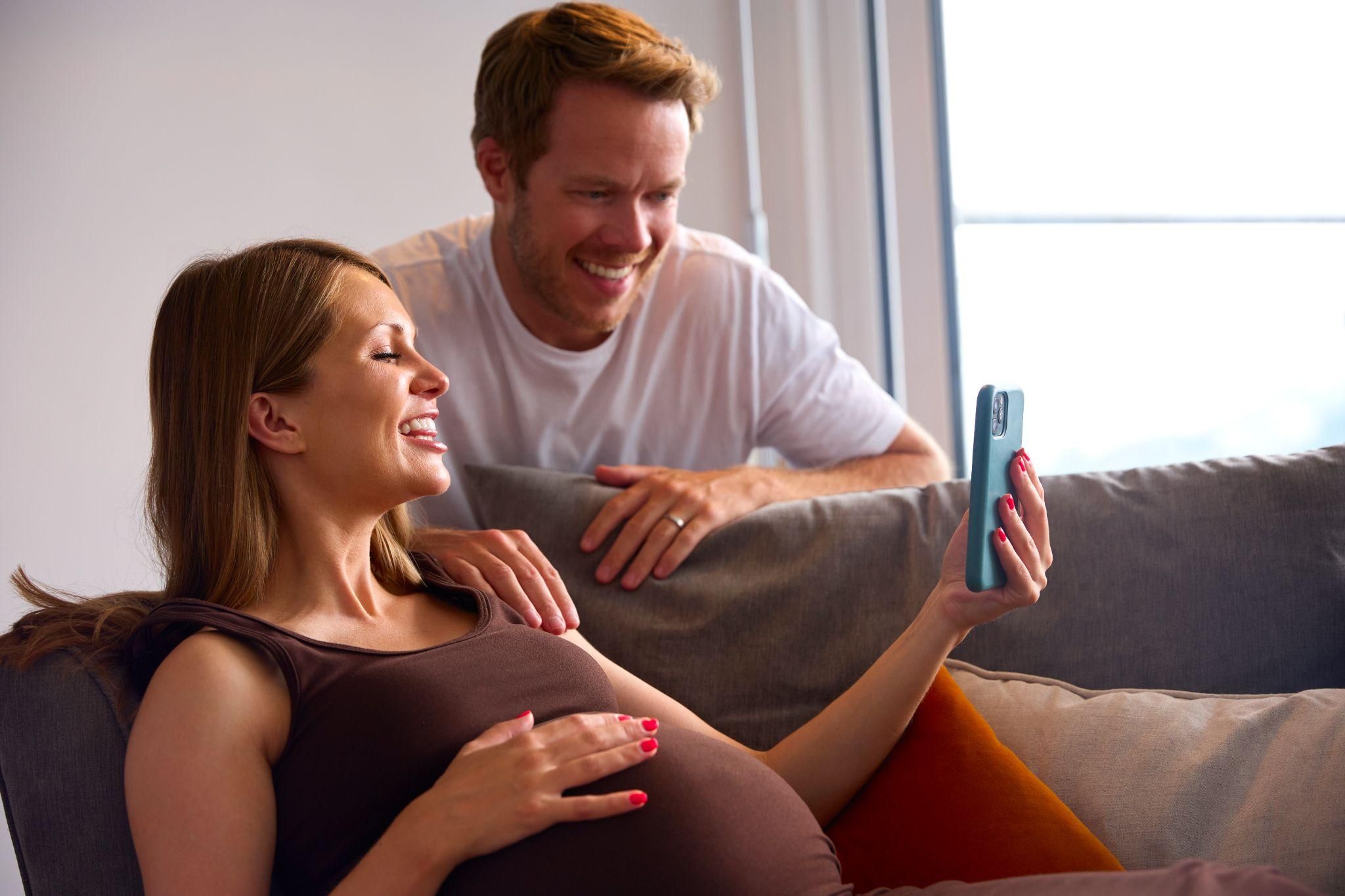 An expectant father smiling as he explores features on a pregnancy app designed for dads.