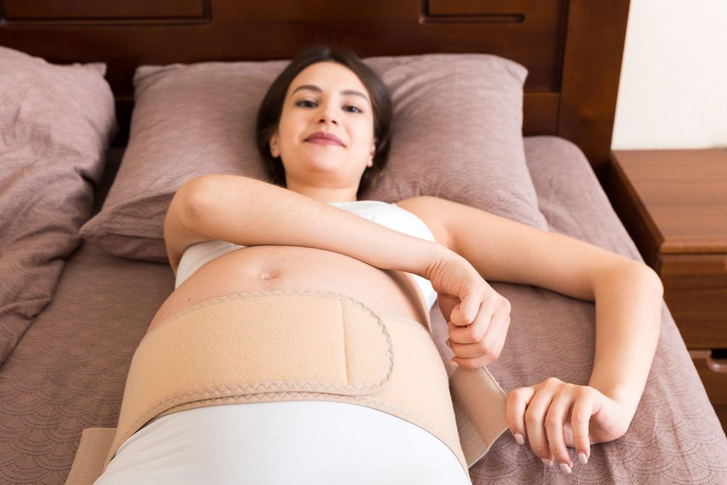 Pregnant woman puts on abdominal support belt to alleviate discomfort.