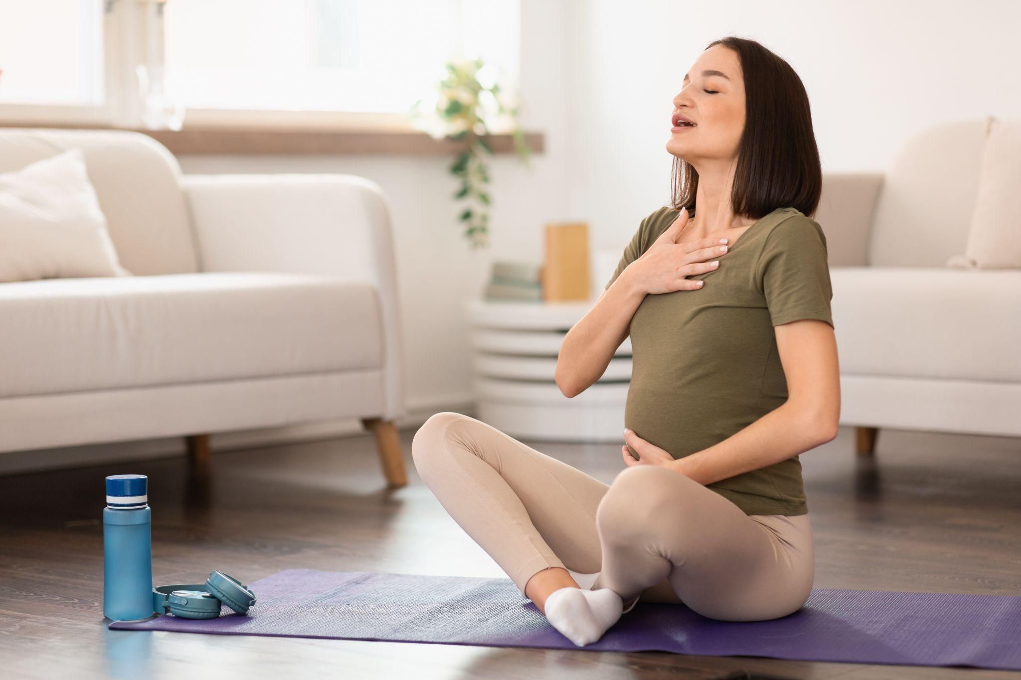 A pregnant woman sitting cross-legged, focusing on deep breathing techniques for relaxation.