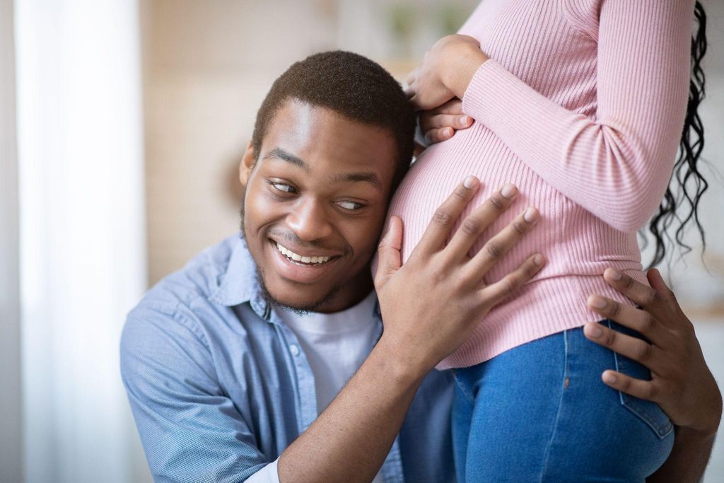 Birth partner listens to pregnant woman’s bump at antenatal class.