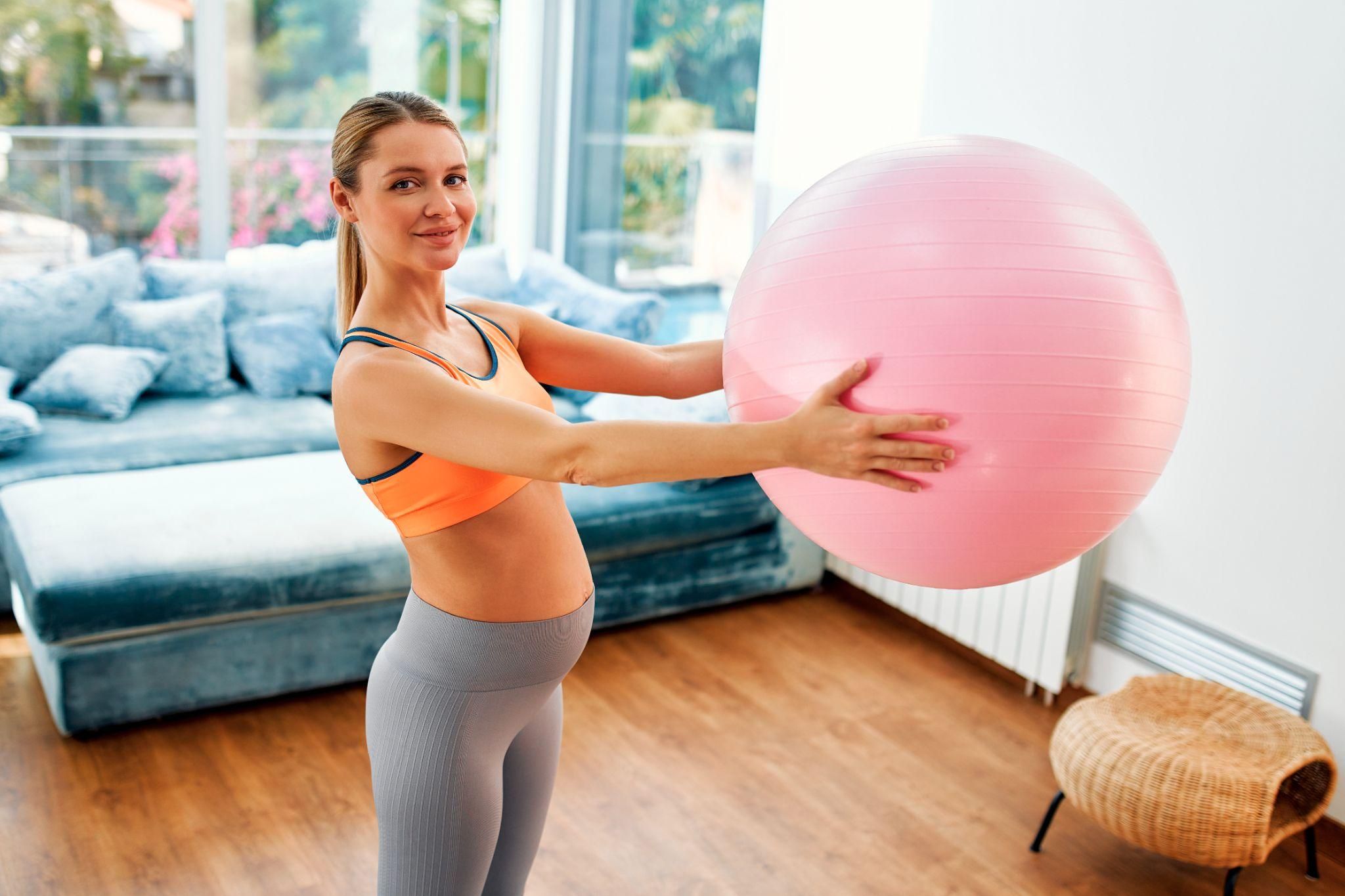 Glowing pregnant woman working out with birthing ball.