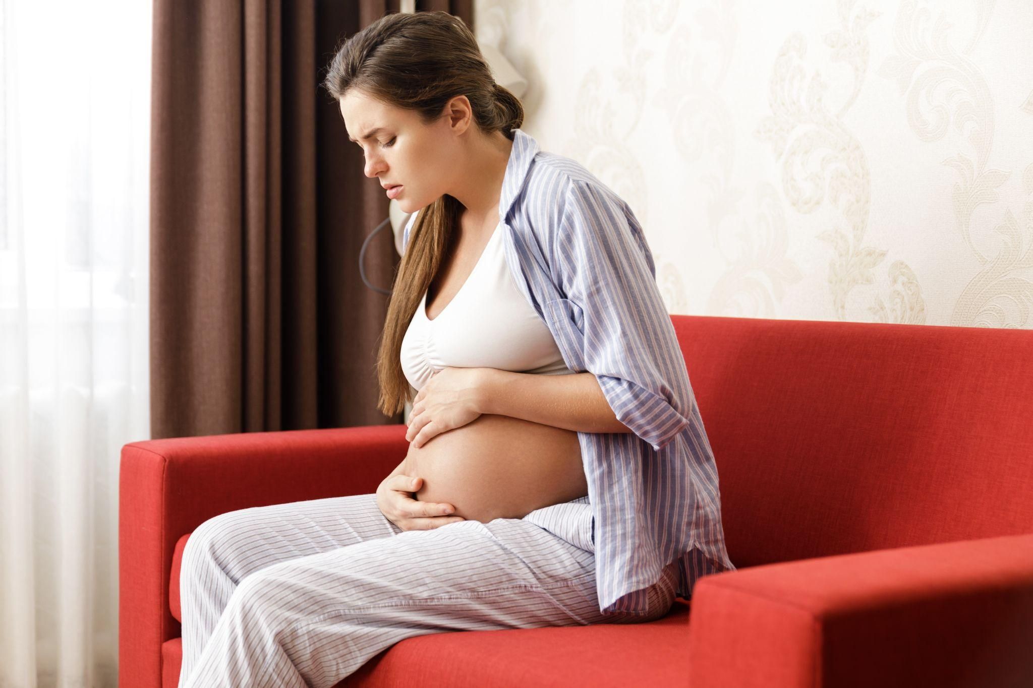 A pregnant woman with pelvic pain sits on her sofa.