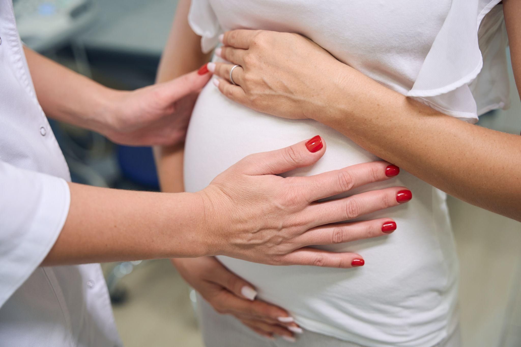 Doctor puts hands on pregnant woman’s bump during appointment at antenatal clinic.