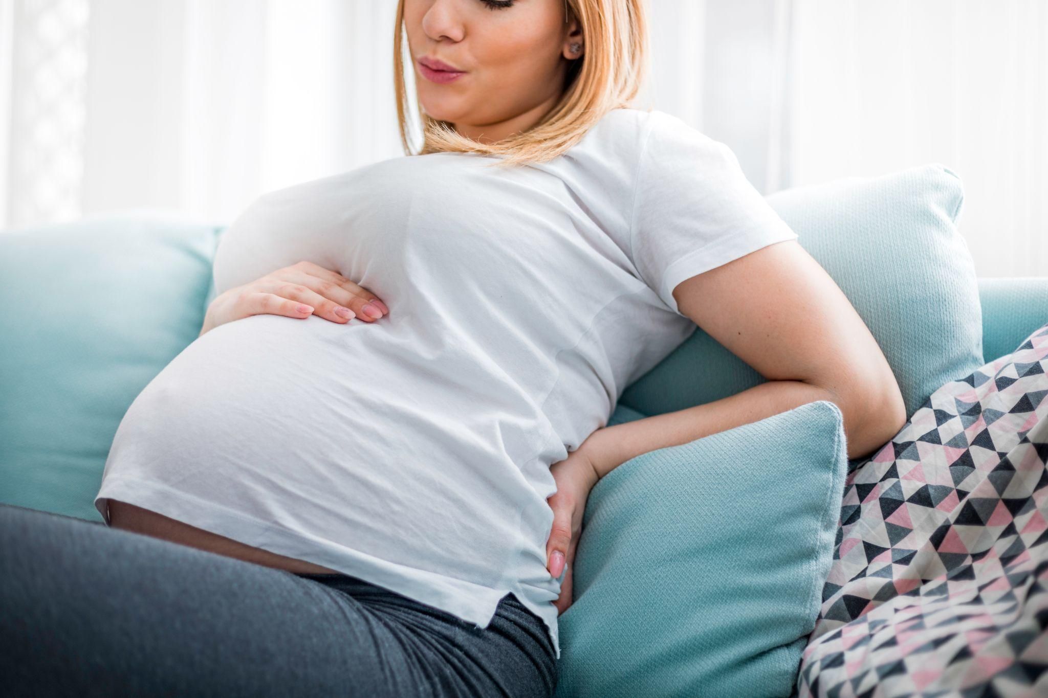 A pregnant woman using a cushion for back cramp relief.