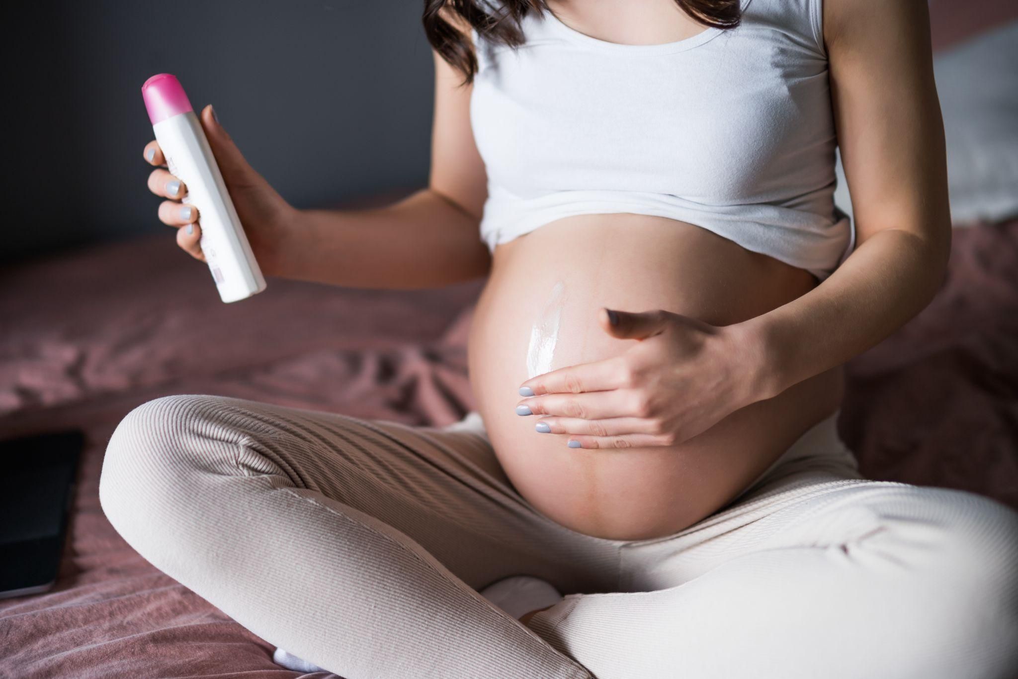 Pregnant woman using body lotion and styling her hair, demonstrating antenatal self-care.