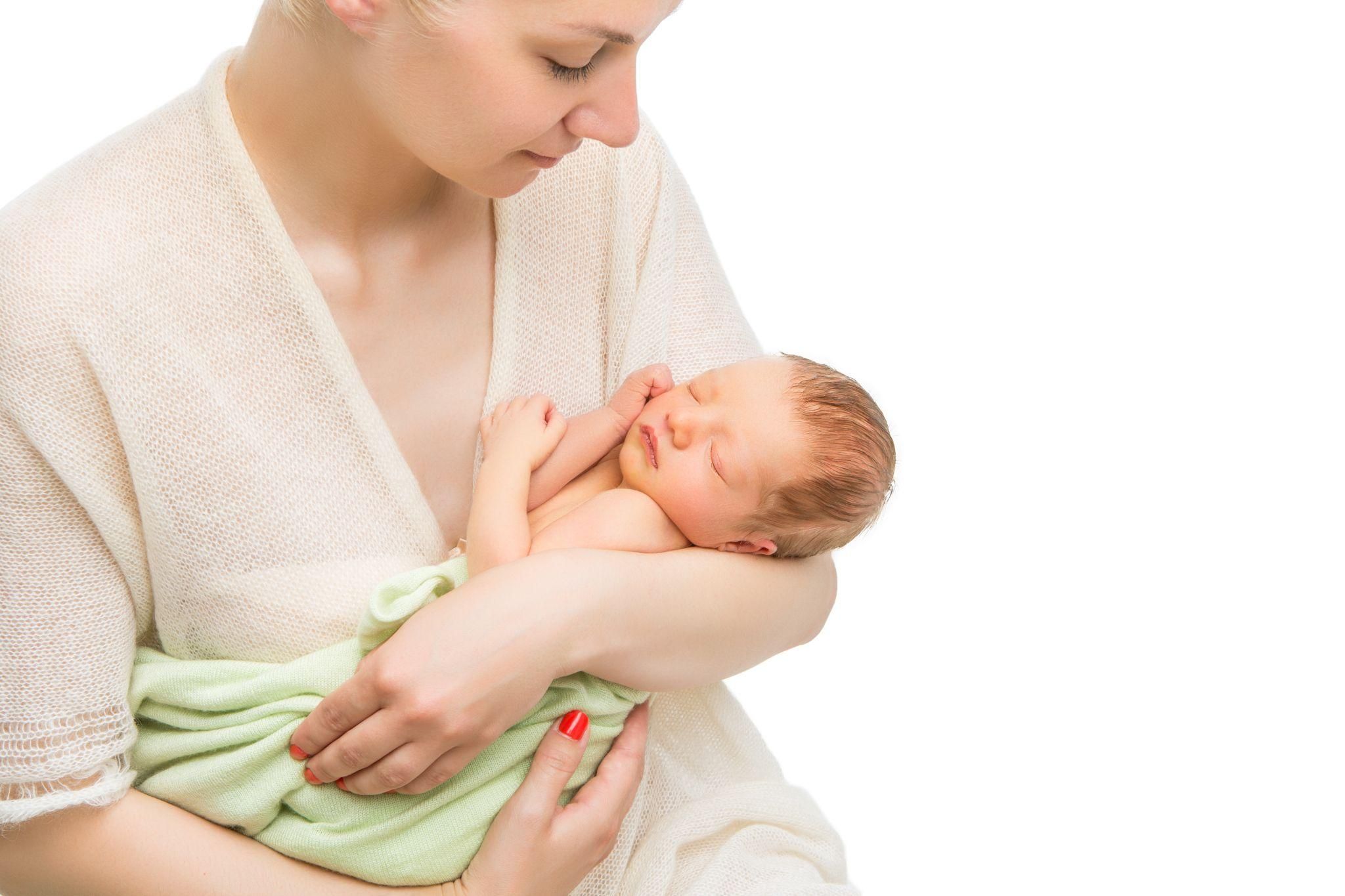 A newborn baby snuggling in a parent’s arms, with tightly curled arms and legs.