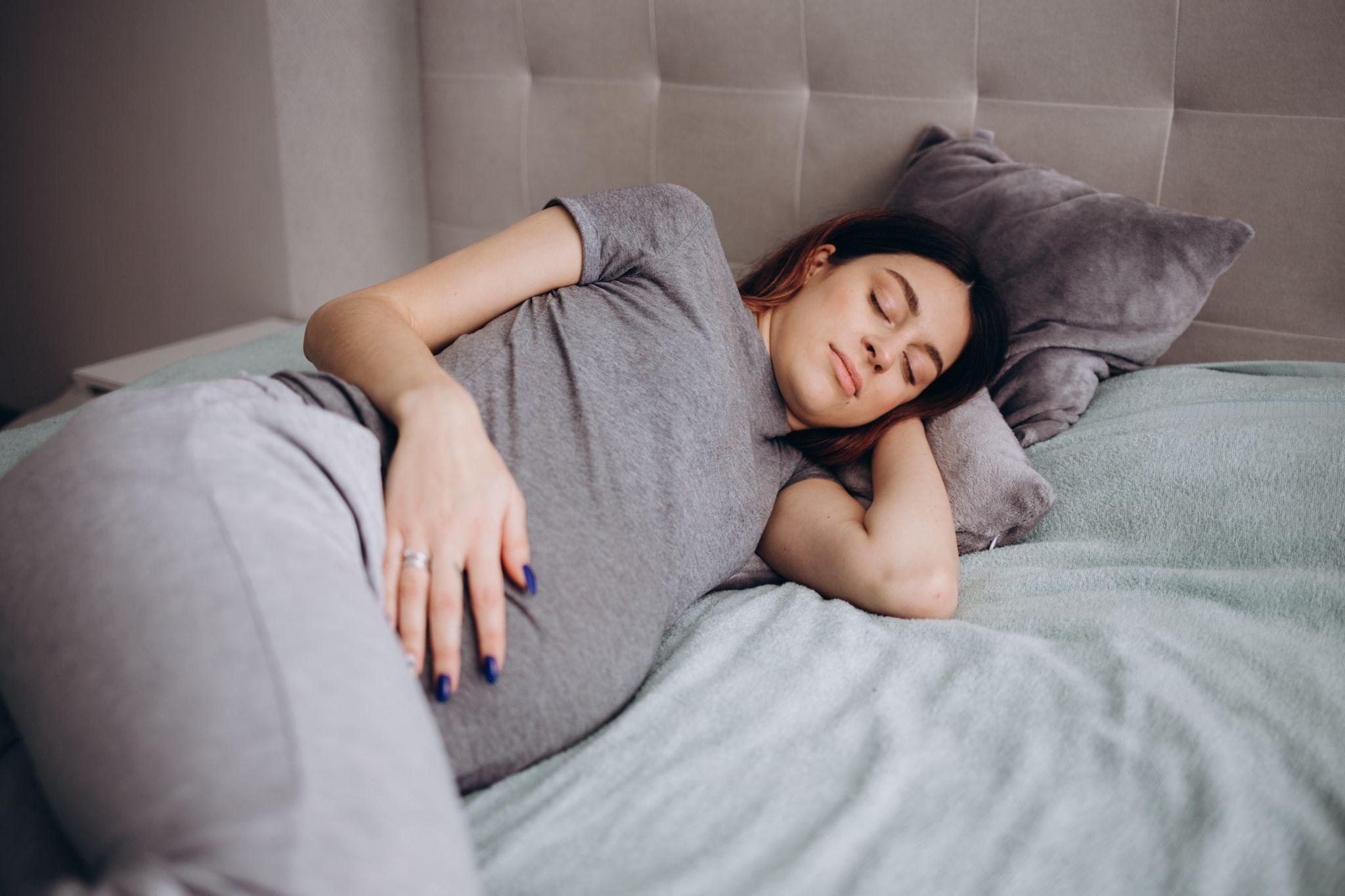 Pregnant woman resting comfortably on her left side with a supportive pregnancy pillow.