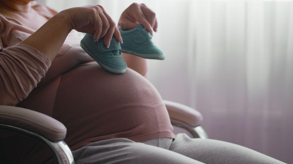 A pregnant woman gently holding her belly, waiting to feel her baby’s first kick.