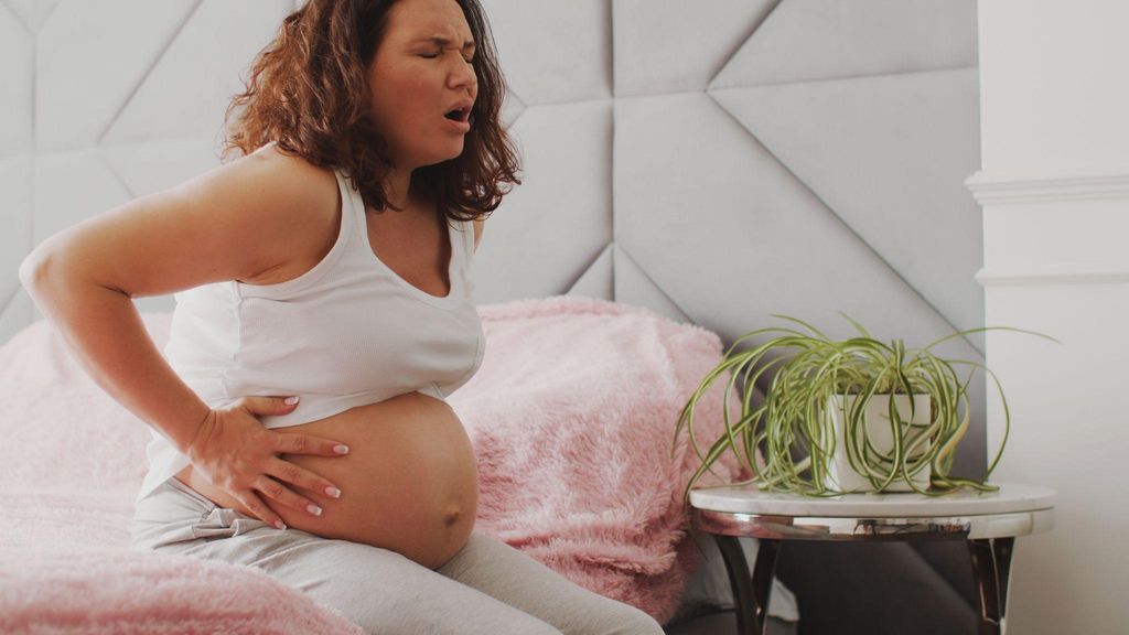 A pregnant woman experiencing discomfort from baby movements, touching her belly.