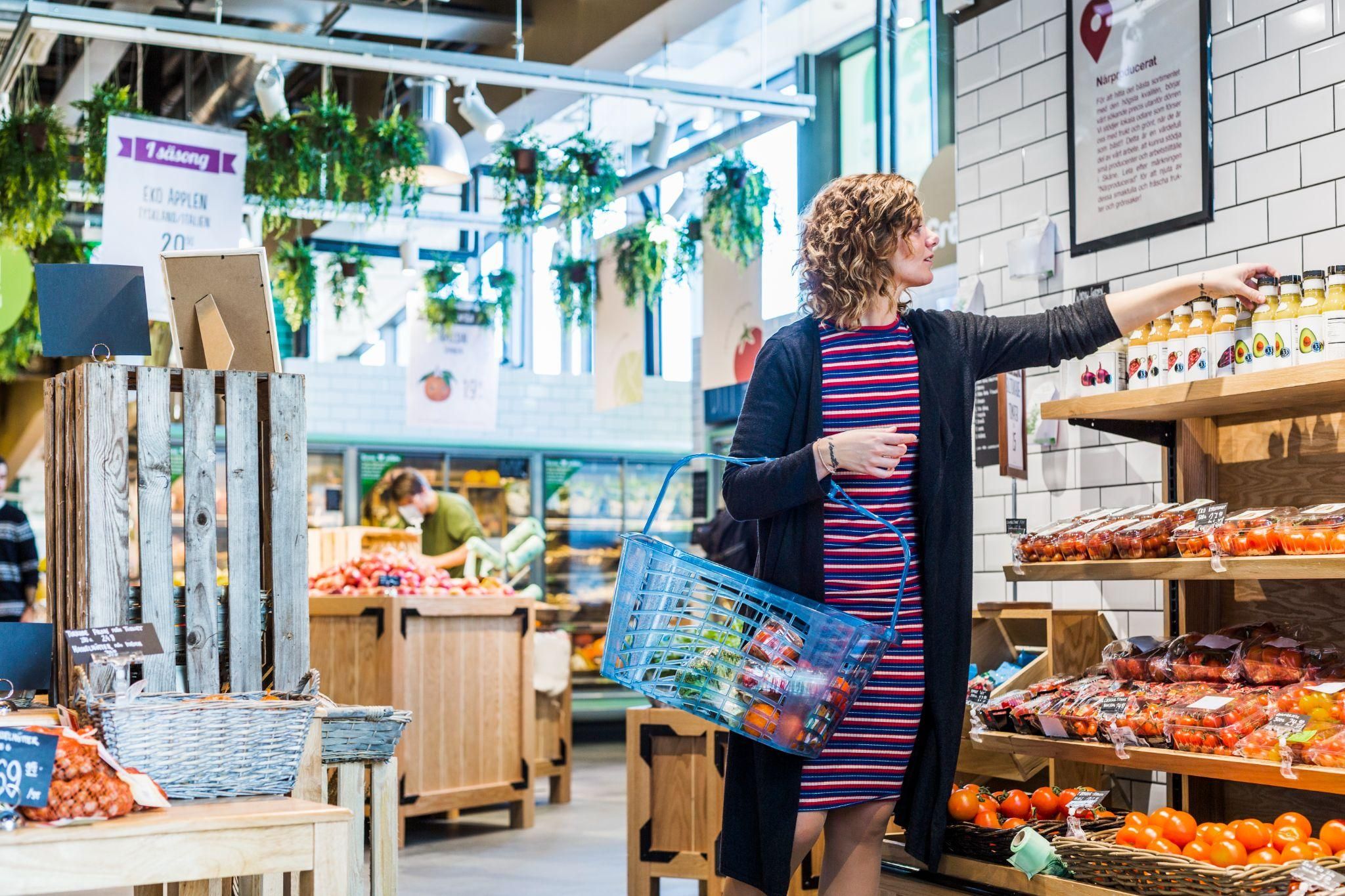 Pregnant woman picking fresh produce from a supermarket, balancing budget and nutrition.