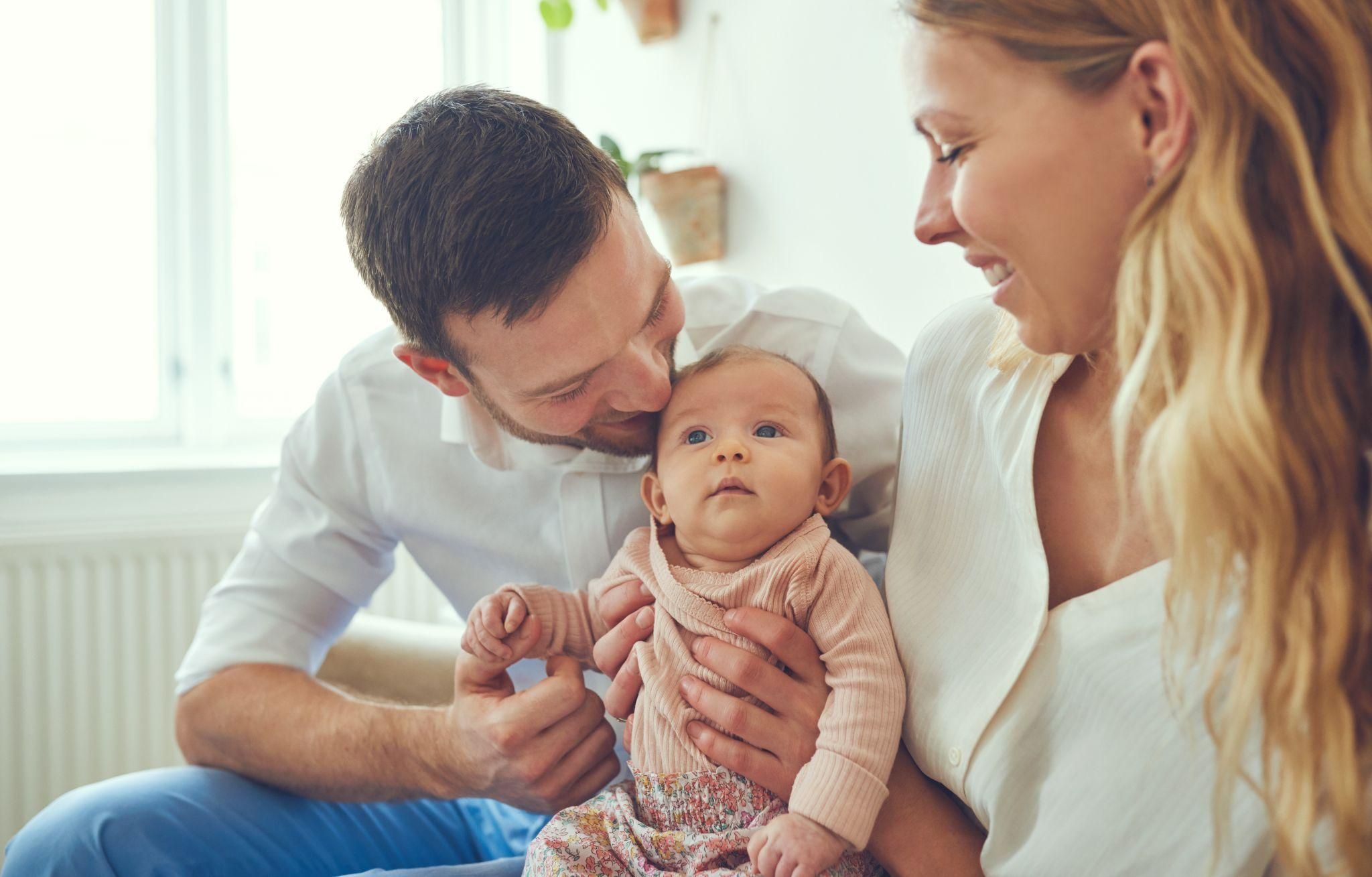 A supportive father bonding with his newborn baby while the mother watches lovingly.