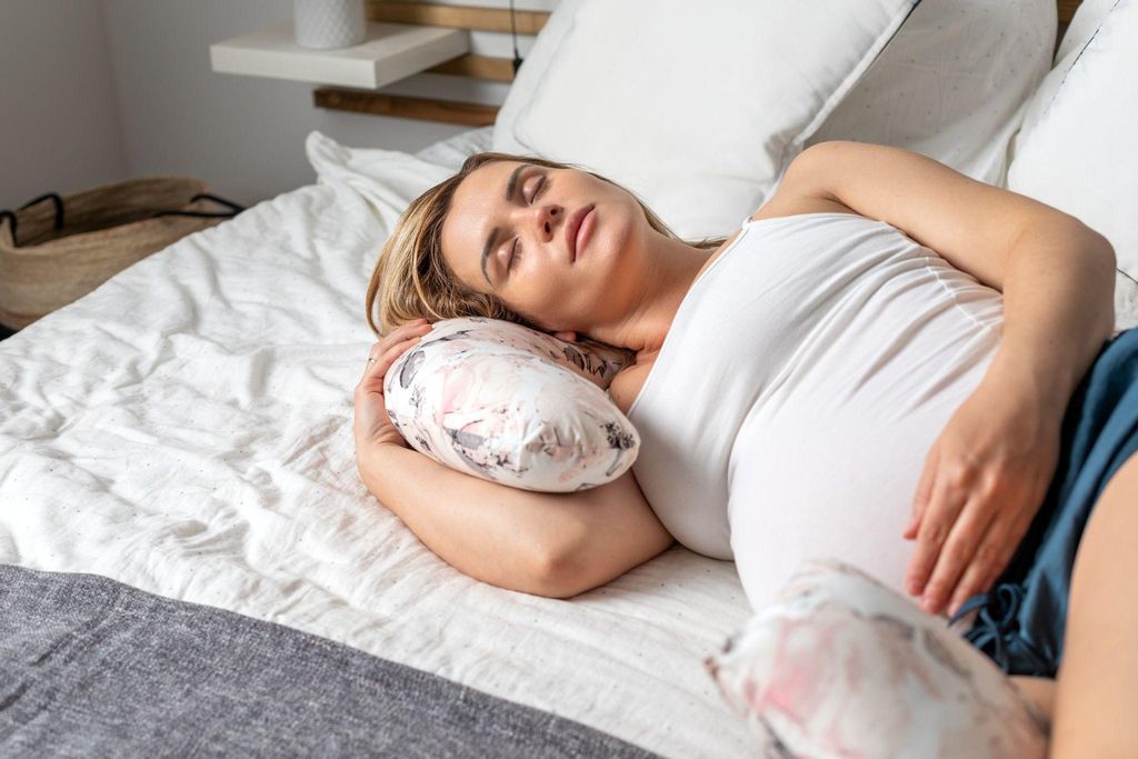 Pregnant woman sleeping on bed in third trimester.