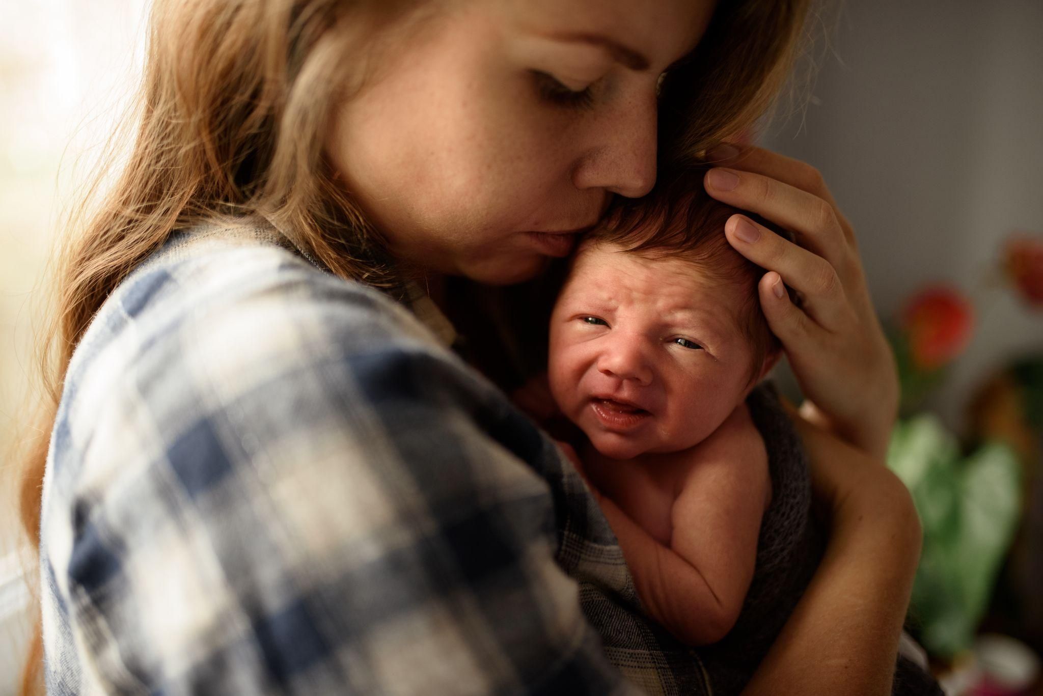 A mother holding her newborn baby and looking reflective, representing the emotional journey of bonding with a newborn.