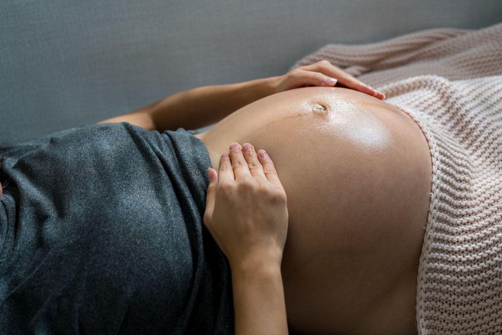 A pregnant woman engages in self-massage of her baby bump as part of her antenatal self-care routine.