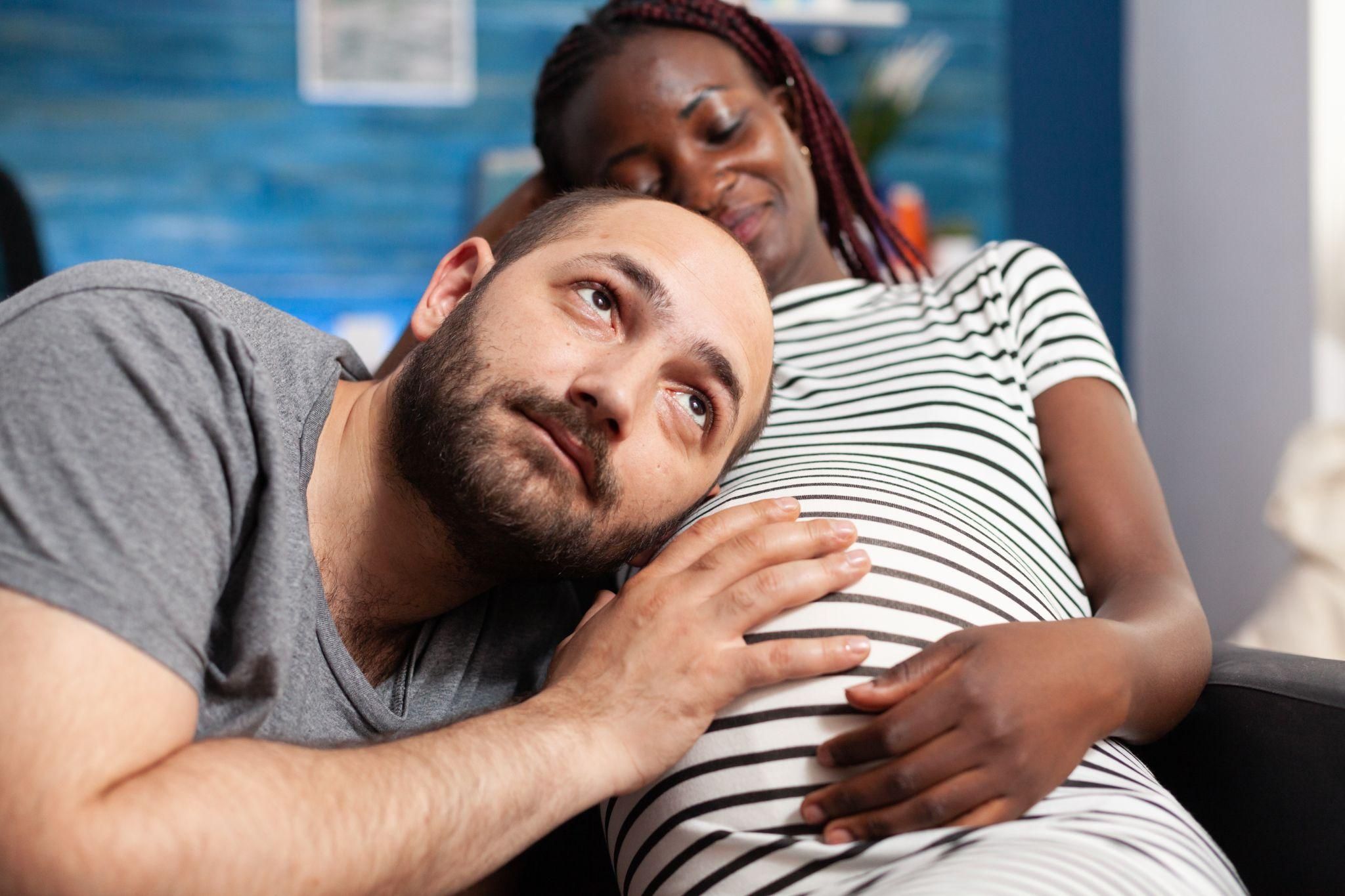 Man listening to pregnant wife’s bump.