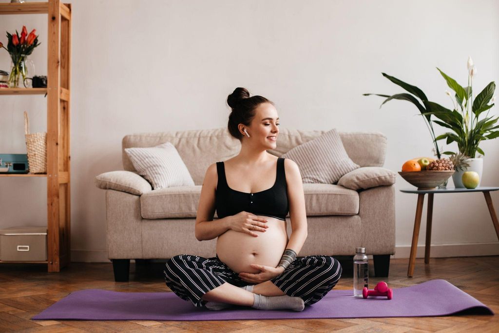 Pregnant woman listening to music while sitting on a yoga mat at home and holding her bump.